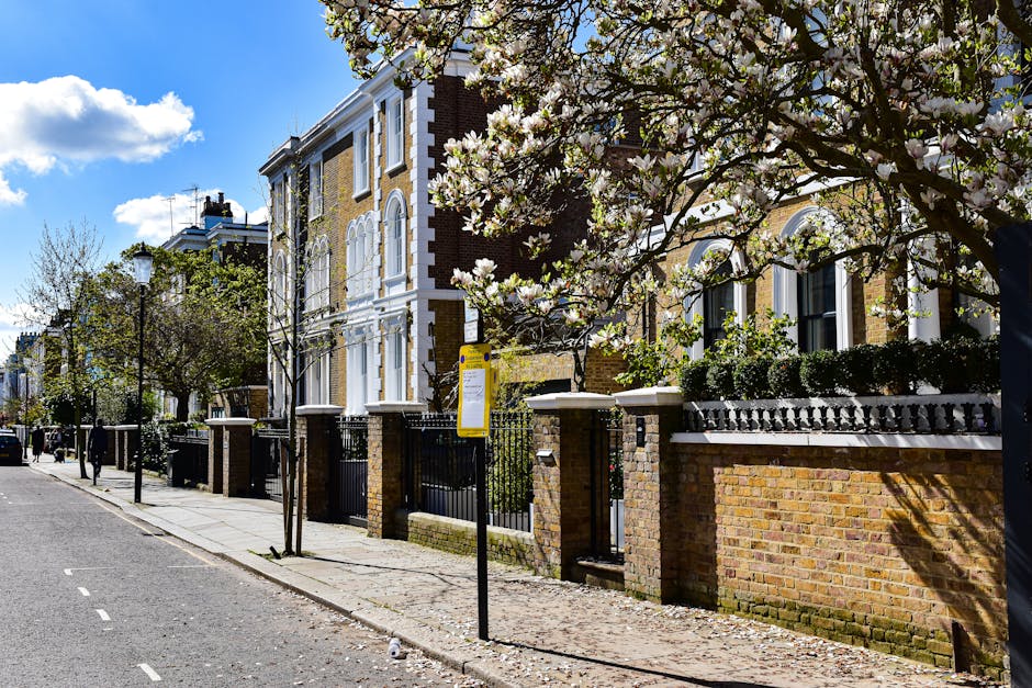 A row of white Victorian-style terraced houses with ornate architectural details, including decorative cornices and ironwork balconies, lining a paved sidewalk in Belgravia. The buildings have black w