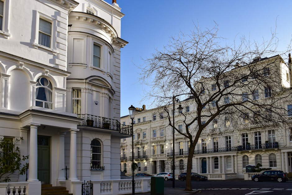 A row of elegant, white multi-storey Victorian-style terraced houses with ornate architectural details, including decorative cornices, window pediments, and wrought iron balconies along the Feltham St